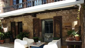 Un espacio al aire libre con sillas blancas y una mesa, rodeado de plantas en macetas y un muro de piedra.