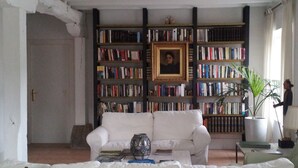 Una sala de estar con un sofá blanco, una estantería llena de libros, un cuadro en la pared y una planta en maceta.