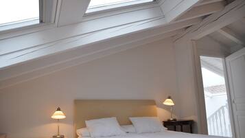 Een slaapkamer met een dakraam, een bed met witte lakens, twee bedlampen en een nachtkastje.