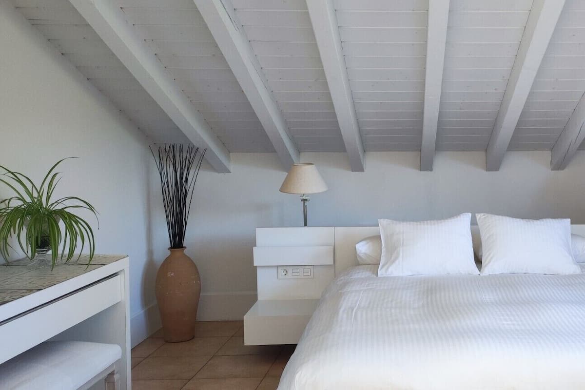 A bedroom with a bed, bedside lamps, a nightstand, a potted plant, and a large vase.