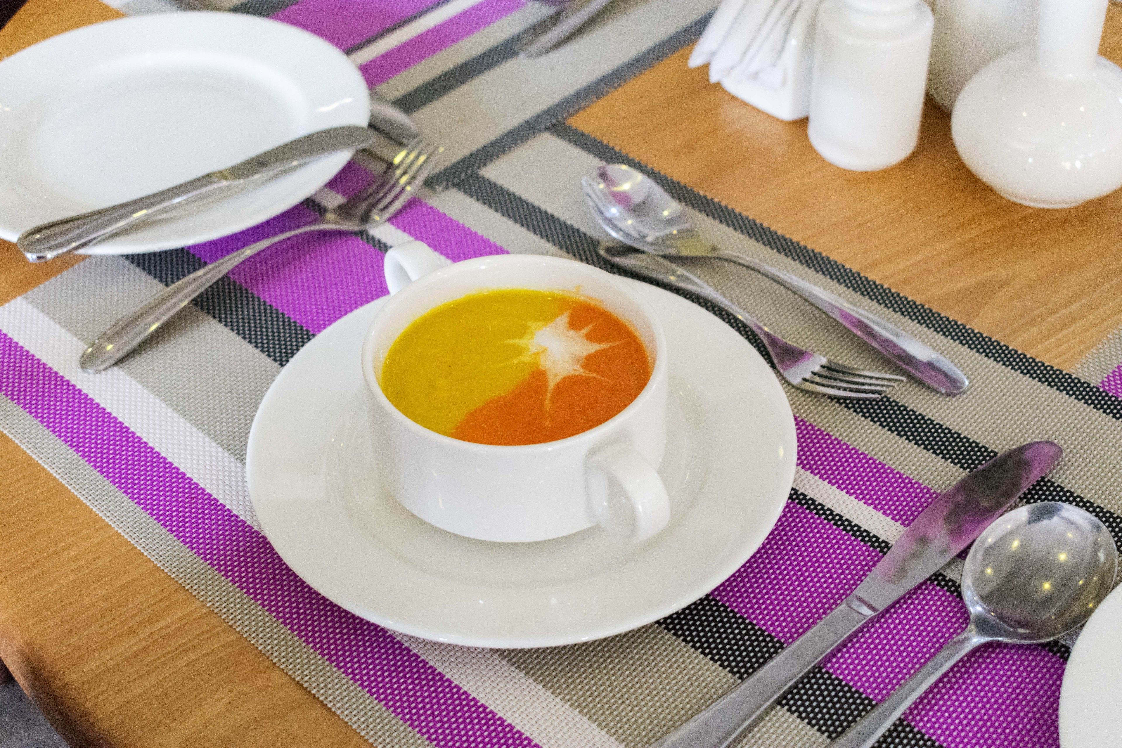 A table set with a white plate, a cup of soup, and cutlery.