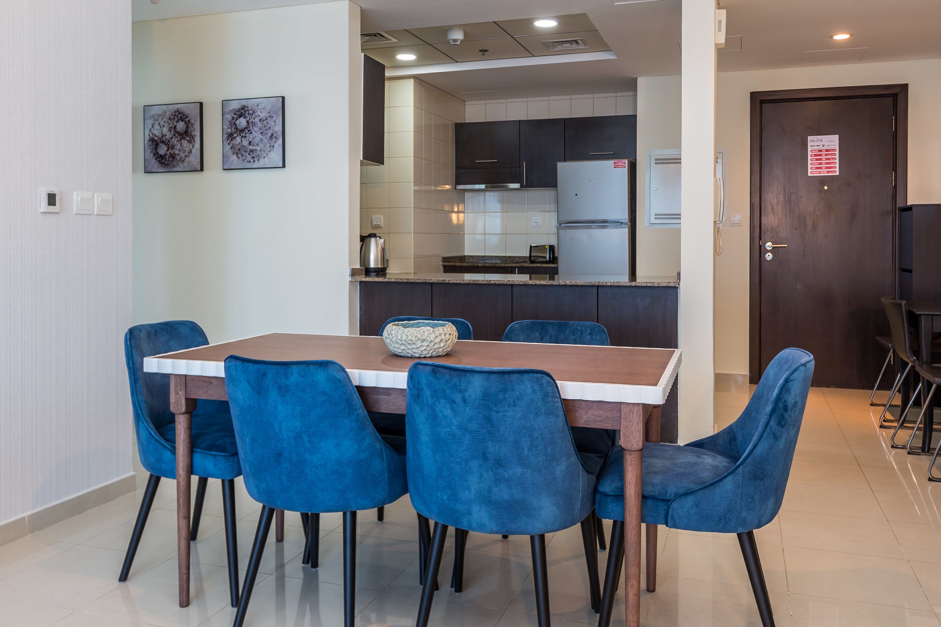 Une cuisine moderne avec des meubles de couleur sombre, un réfrigérateur en acier inoxydable et un coin repas comprenant une table en bois et des chaises bleues.
