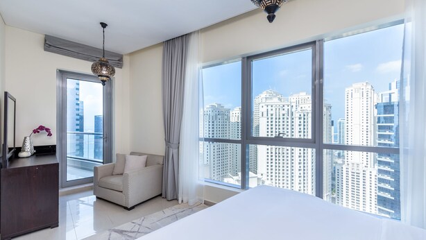 Una habitación de hotel moderna con un ventanal grande que ofrece vistas a la ciudad, una cama, un escritorio y una silla.