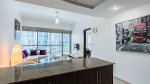 Una cocina moderna con encimera de granito, armarios oscuros, un comedor con mesa redonda y sillas, y un ventanal con vistas a edificios.