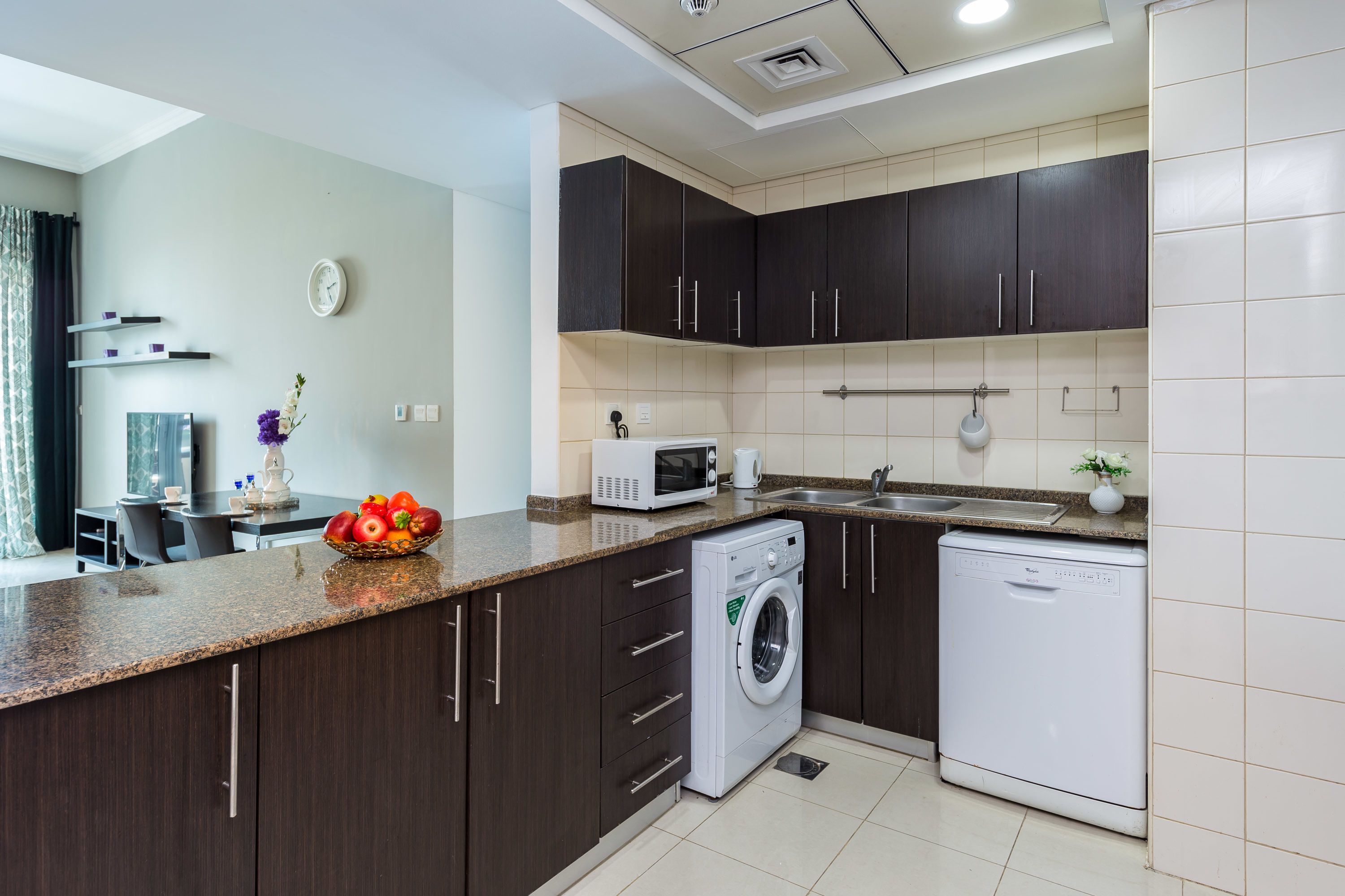 Una cocina moderna con armarios de madera oscura, microondas integrado, lavadora y lavavajillas.