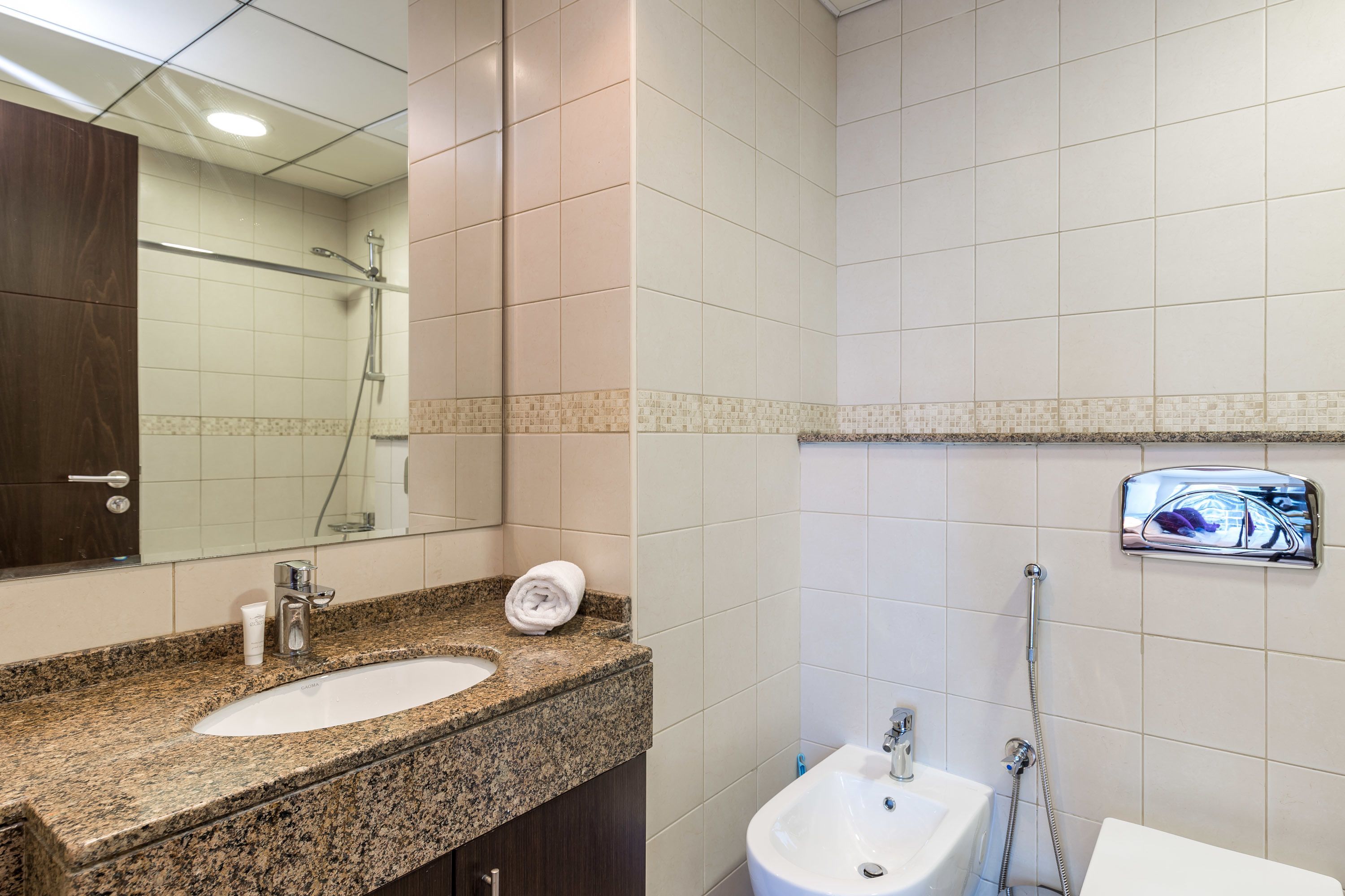 A bathroom with a granite countertop, a sink, a mirror, a shower, and a toilet.