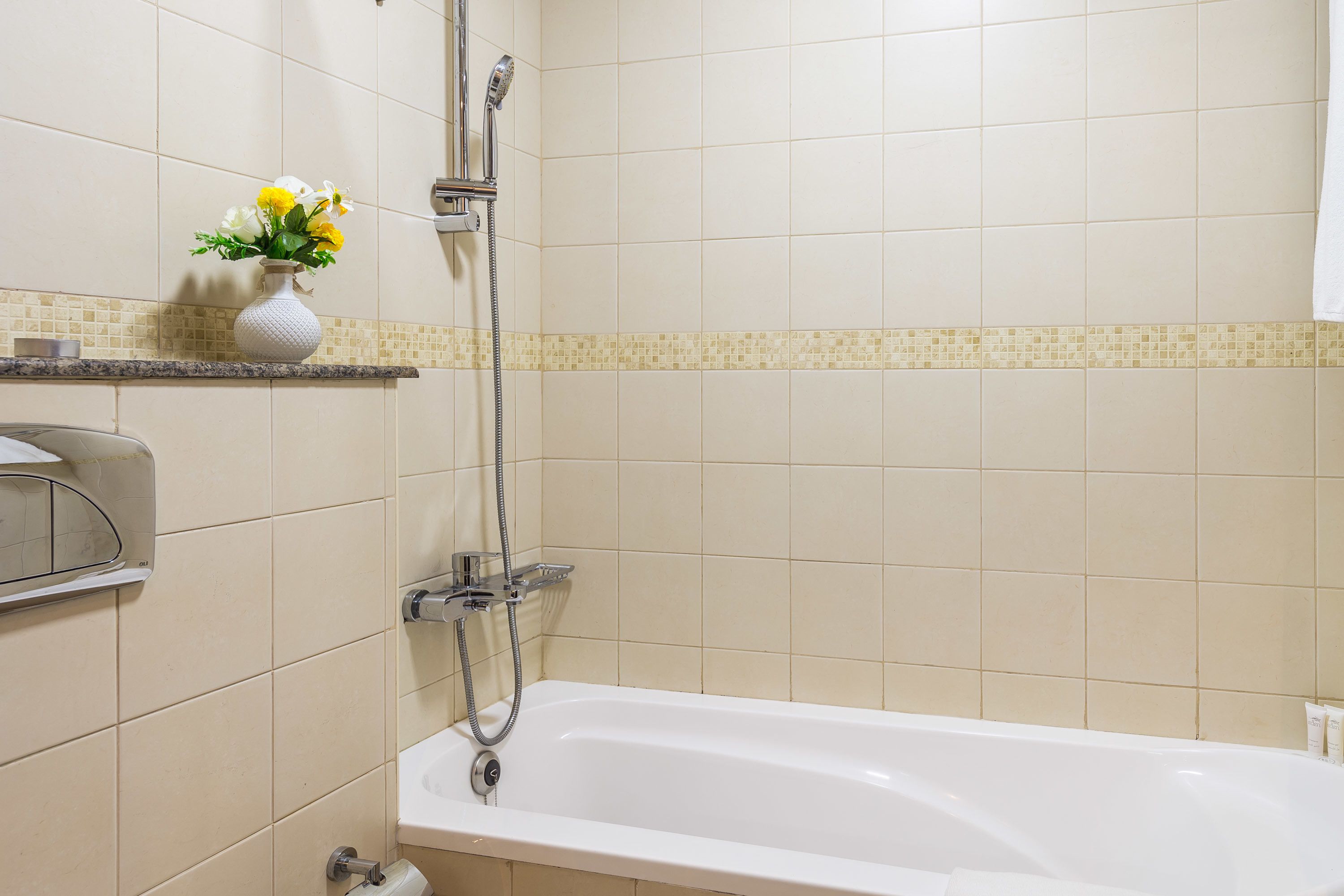 Un baño con bañera, ducha y un florero con flores en un estante.