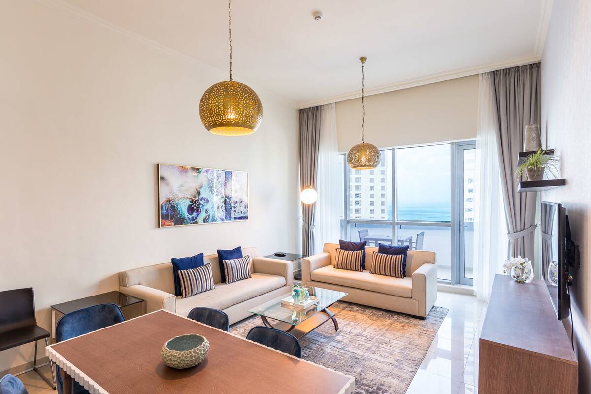 A modern living room with a sofa set, a dining table, and hanging pendant lights.