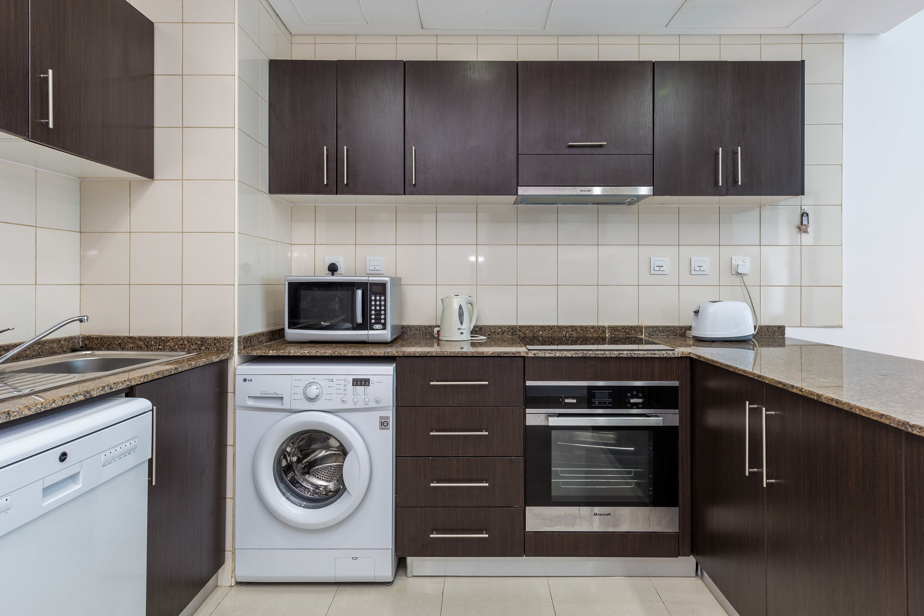 Una cocina moderna con armarios de madera oscura, microondas integrado, lavadora y horno.
