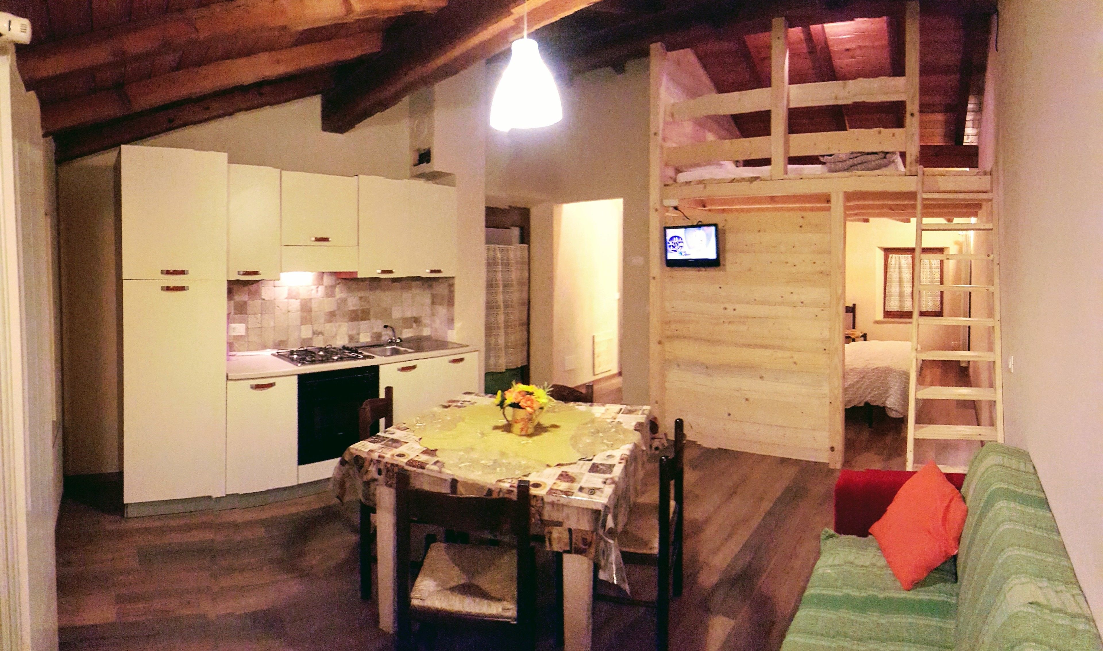 A compact kitchen with white cabinets, a dining table with a floral centerpiece, and a wooden ceiling.