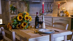 Une table à manger dressée avec une bouteille de vin, des verres, une bougie et un centre de table composé de fleurs.