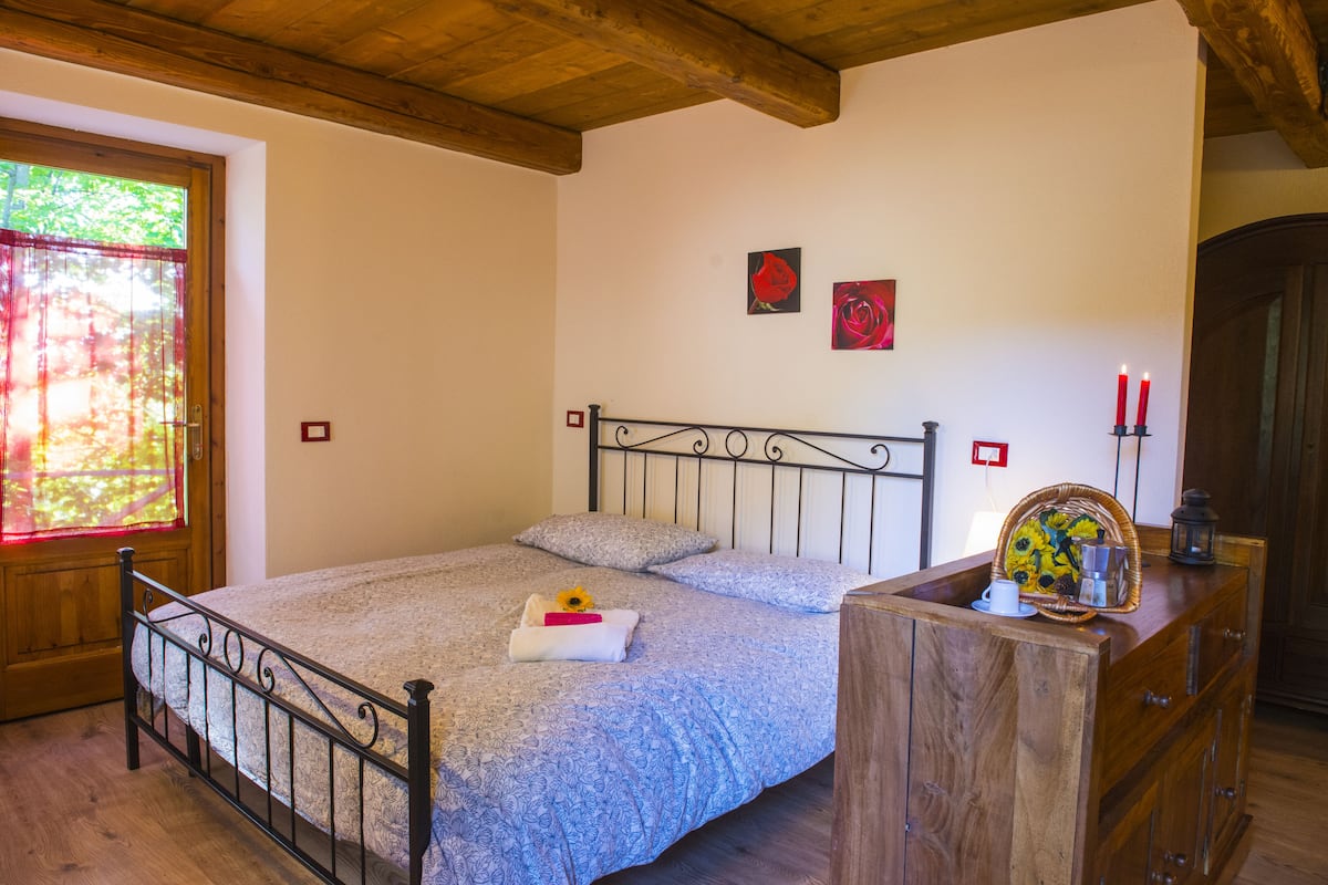 Une chambre à coucher avec un lit, une commode en bois et une fenêtre donnant sur des arbres.