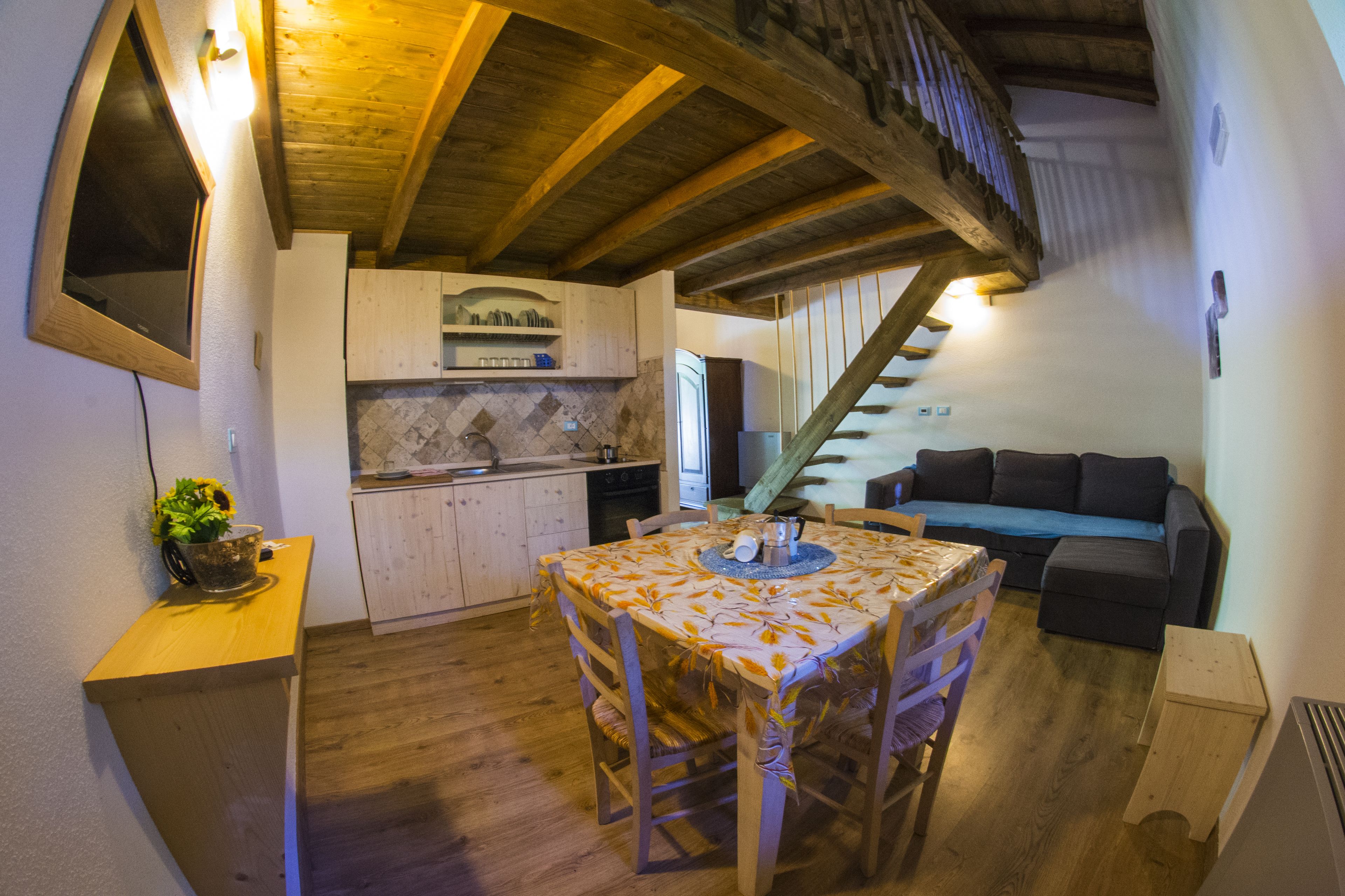A cozy kitchen with wooden beams, a dining table with chairs, and a staircase leading to a loft area.