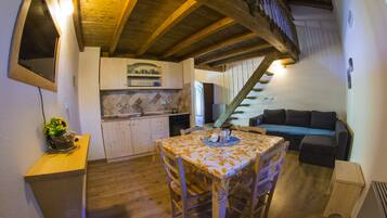 A cozy kitchen with wooden beams, a dining table with chairs, and a staircase leading to a loft area.