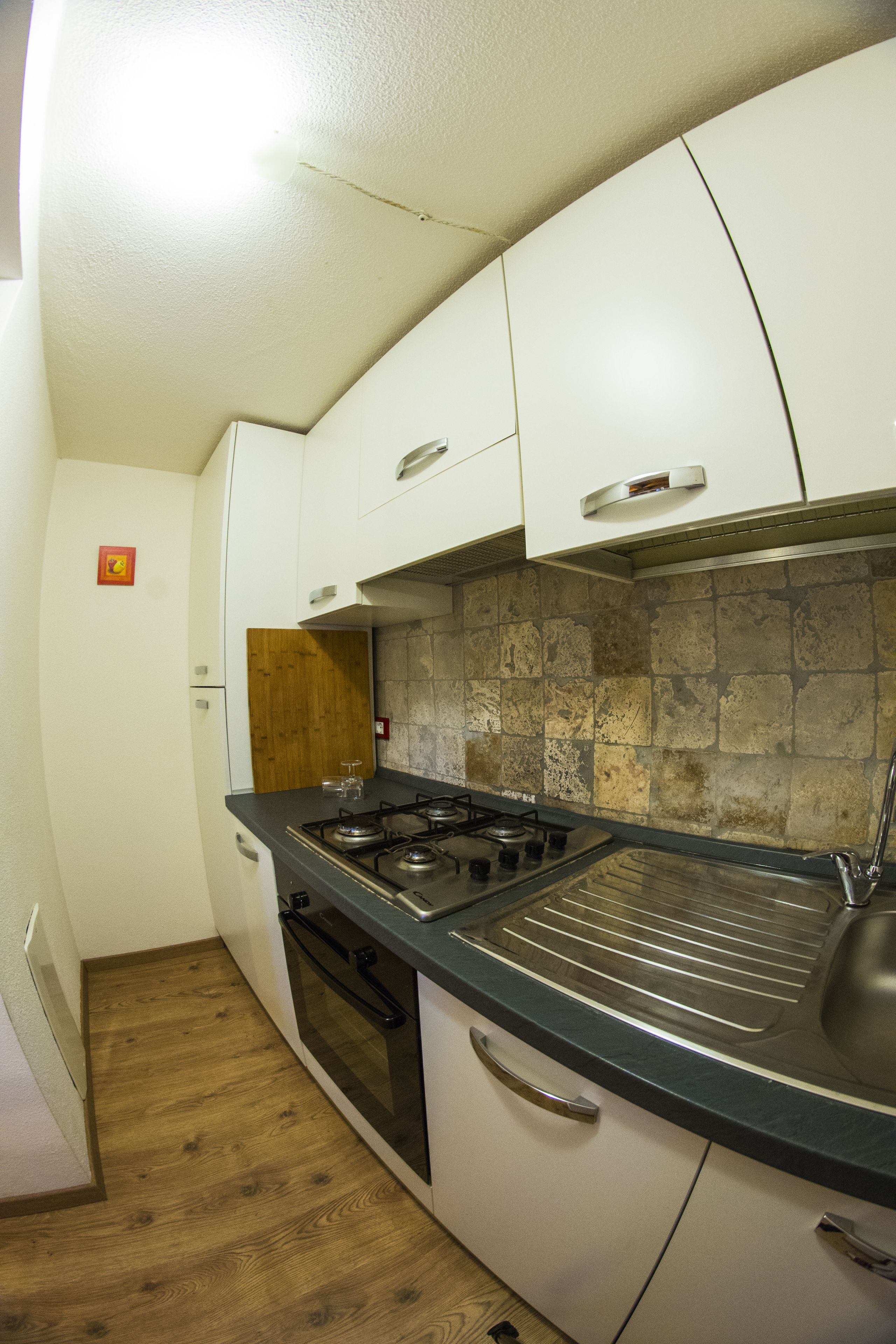 A compact kitchen with white cabinets, a gas stove, and a stone backsplash.