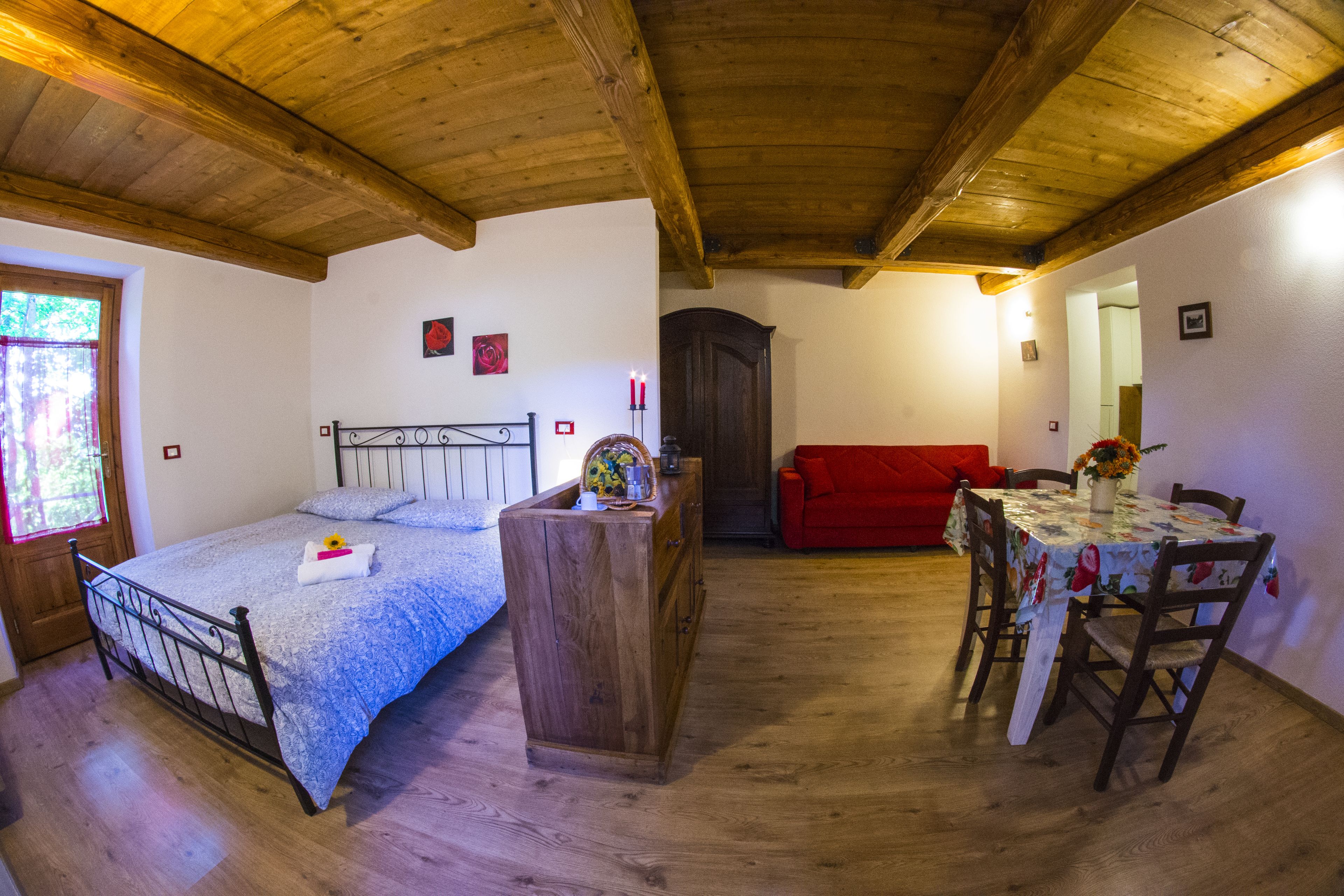 A bedroom with a wooden bed, a dresser, a red sofa, and a dining table with chairs.