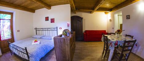 A bedroom with a wooden bed, a dresser, a red sofa, and a dining table with chairs.