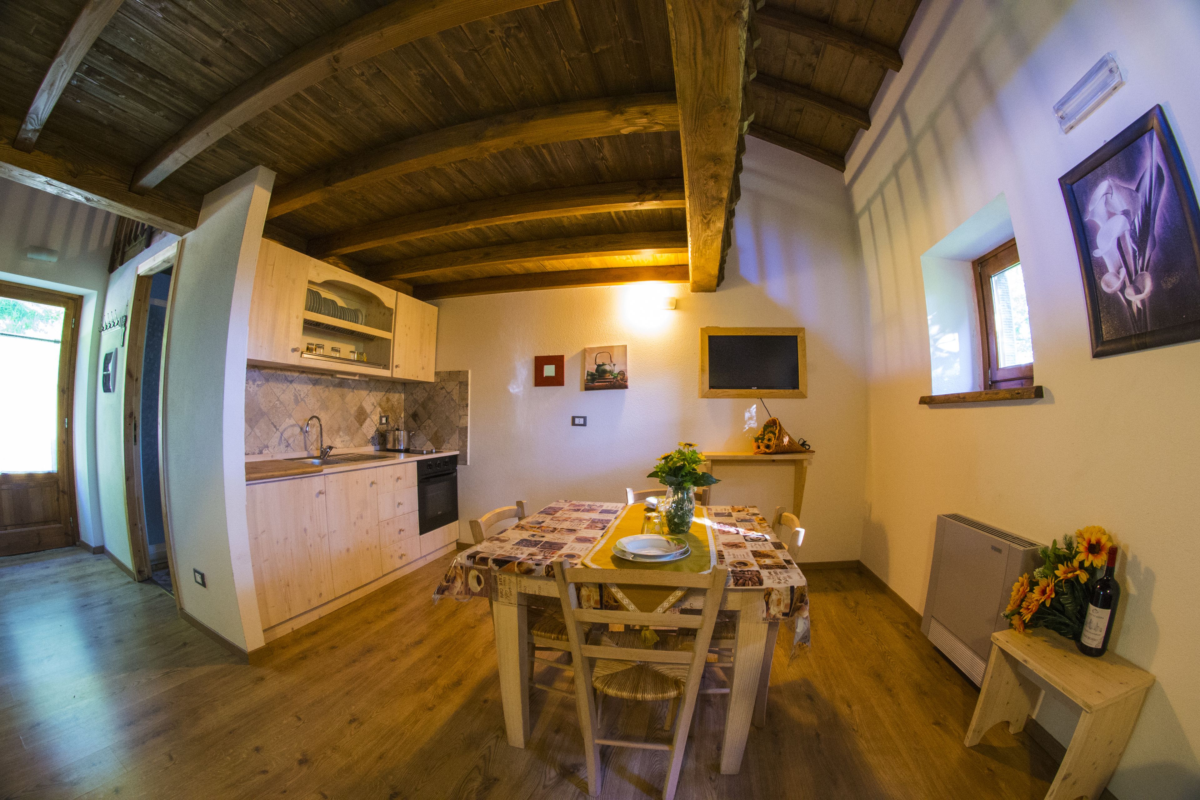 Eine rustikale Küche mit Holzbalken, einem Esstisch mit Stühlen, einem kleinen Kühlschrank und einem Fenster mit Aussicht.