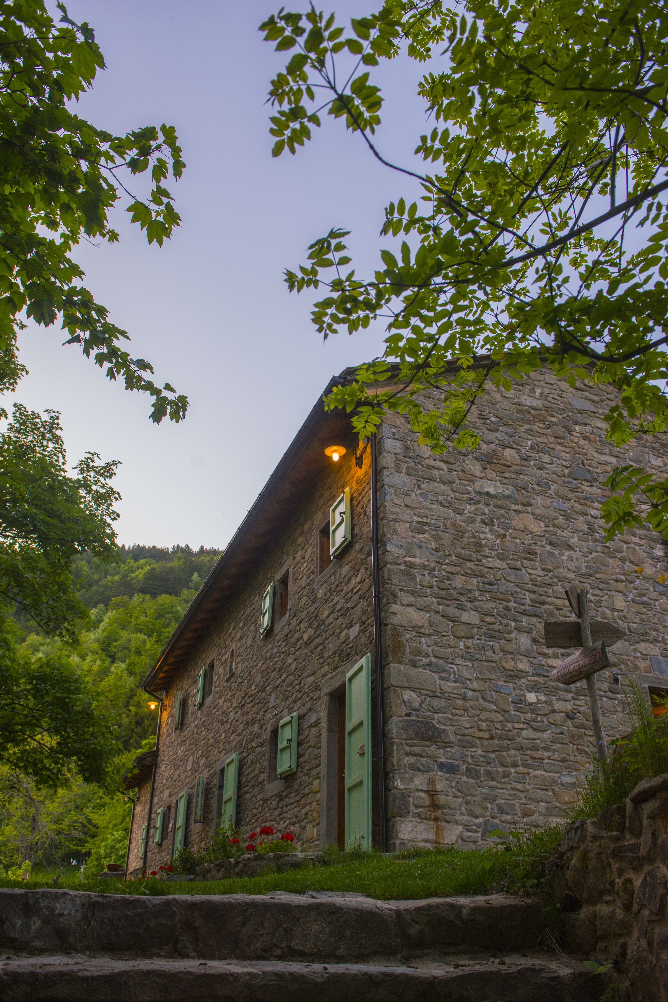 Ein Gebäude aus Stein mit einem geneigten Dach, grünen Fensterläden und einer kleinen Veranda mit Blumen.