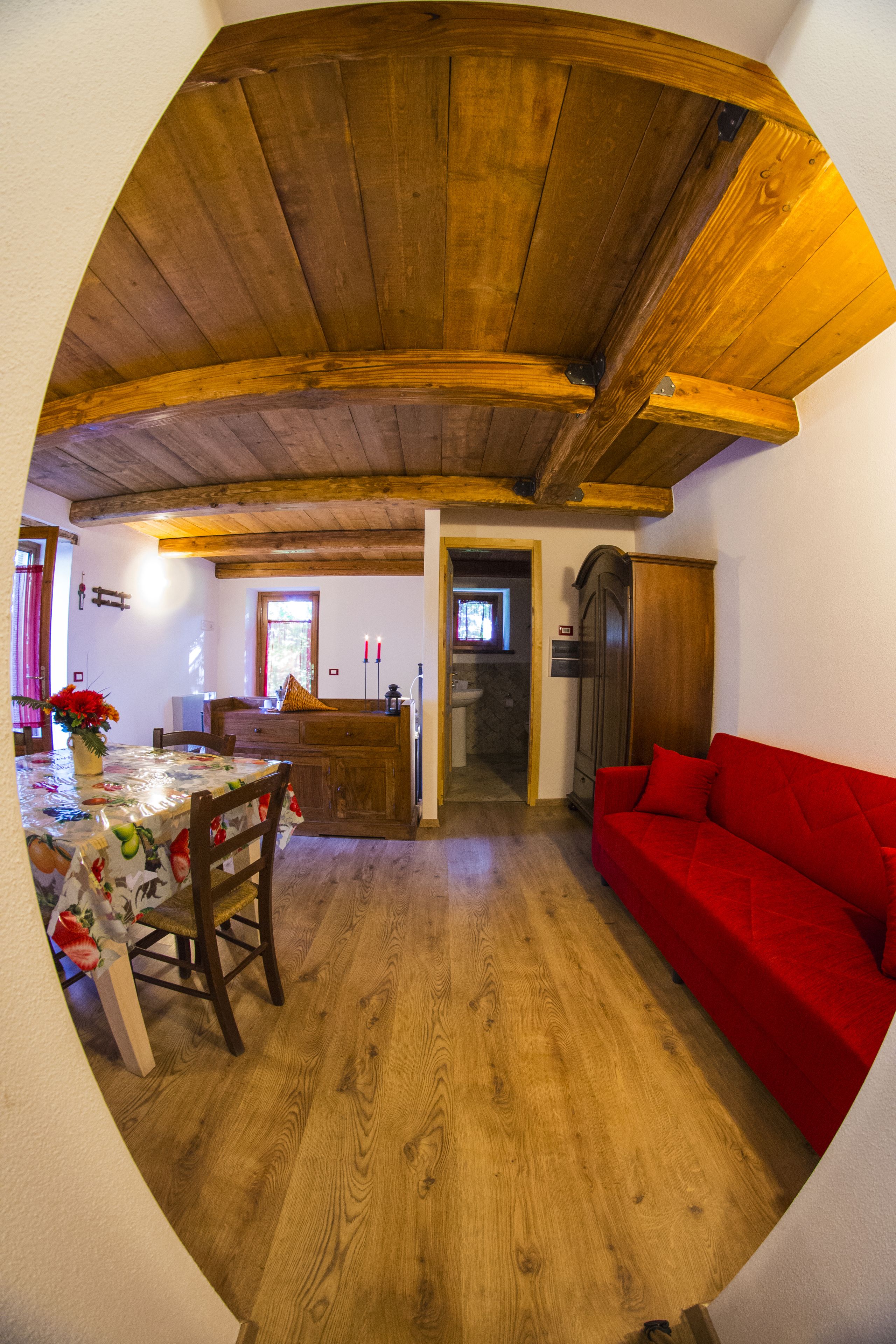 Un comedor con techo de madera, un sofá rojo y una mesa con mantel floral.