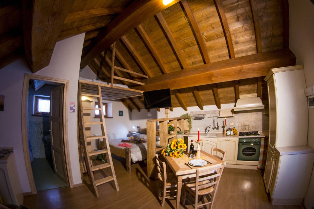 Une cuisine rustique avec des poutres en bois, une table à manger dressée pour deux personnes et un petit coin cuisine.