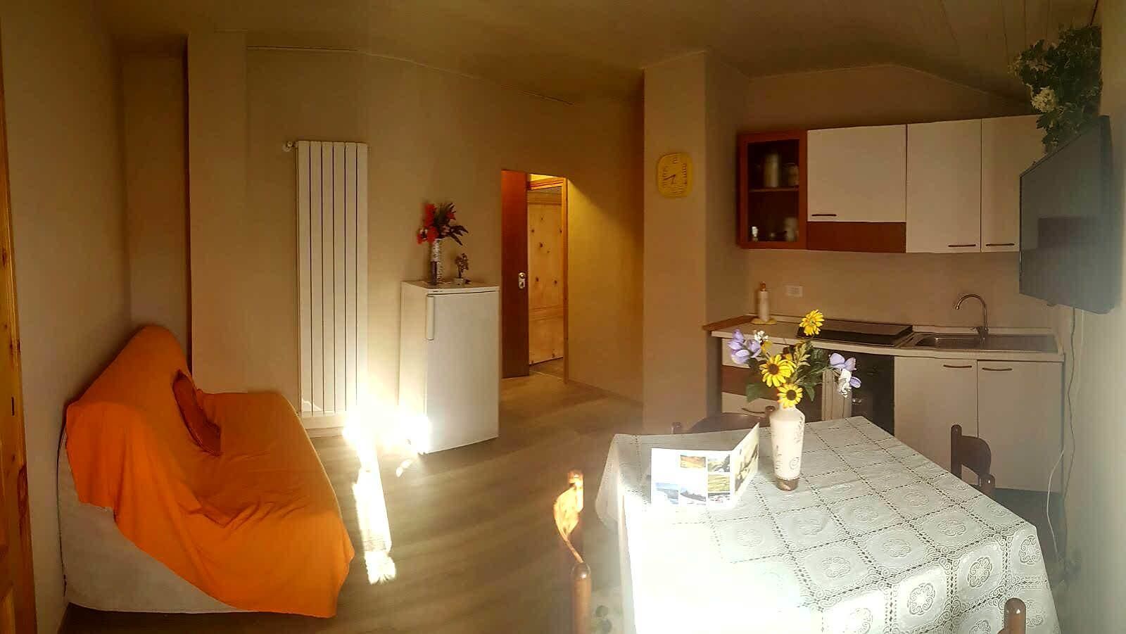 Een ruimtelijk ingerichte leefruimte met een bed, een kleine kitchenette en een eethoek.