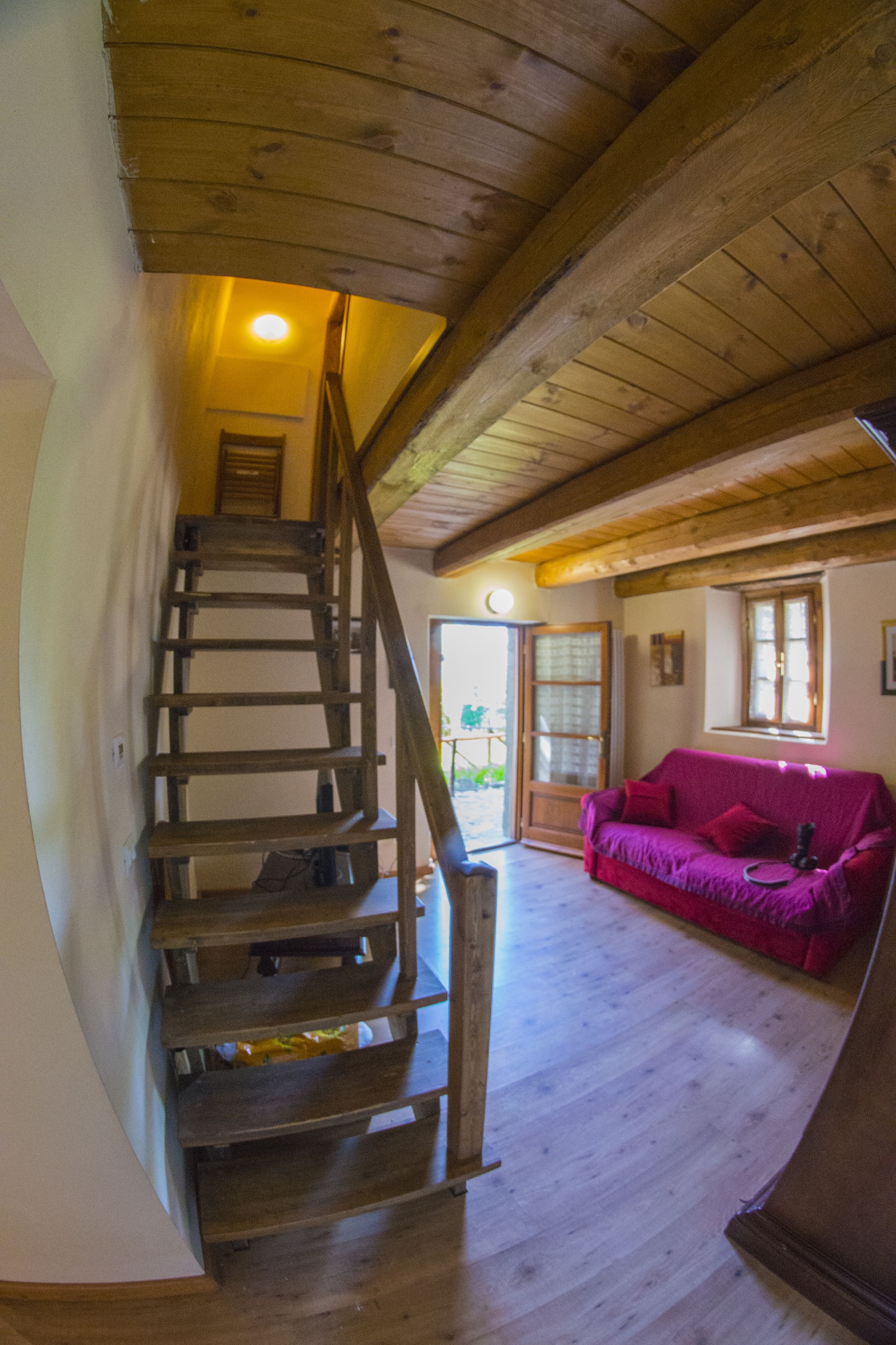 Una escalera de madera que lleva a una habitación con un sofá rojo y una puerta al exterior.