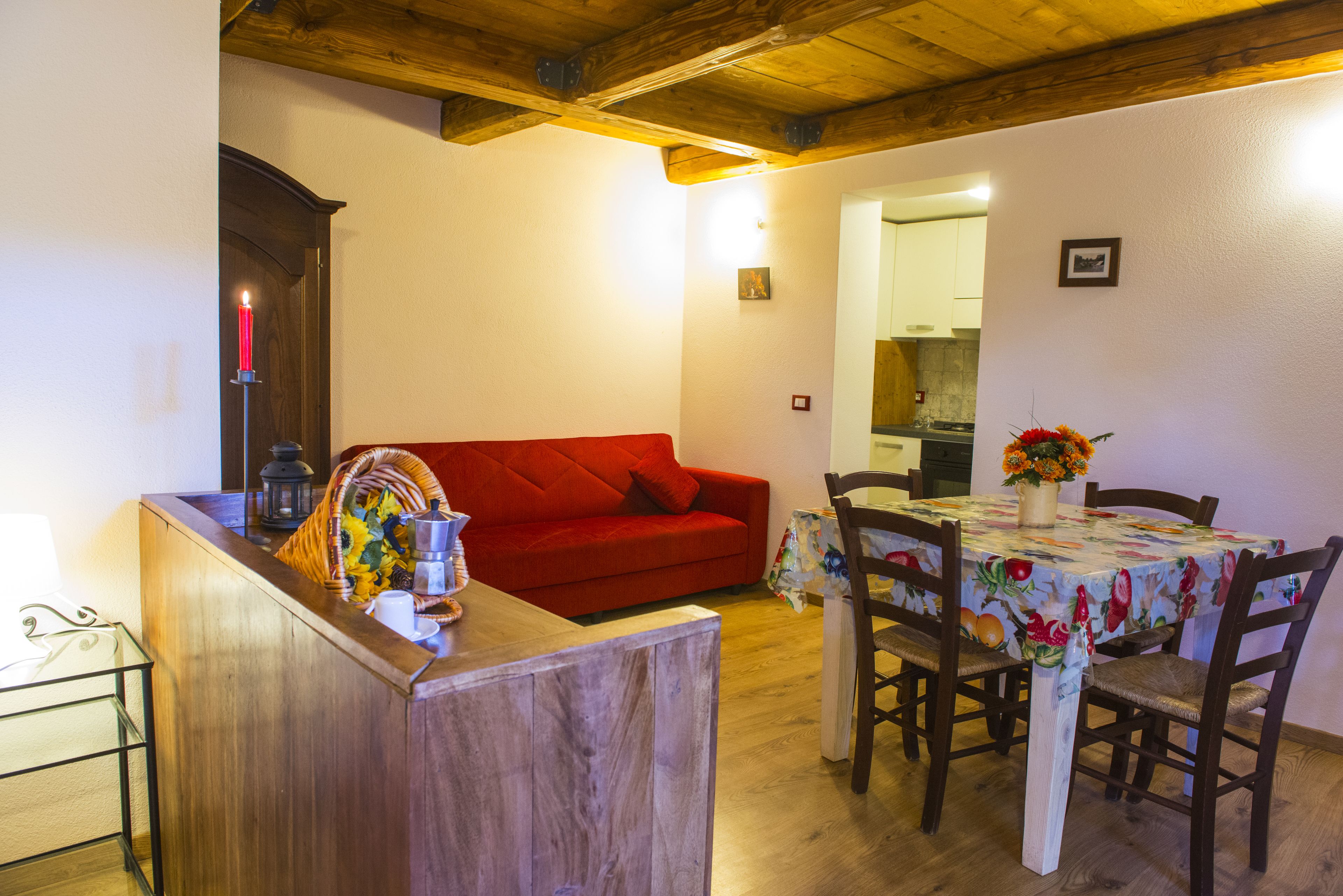 Un espacio de estar acogedor con techo de madera, un sofá rojo, una mesa de comedor con sillas y un florero con flores.
