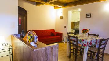 Un espacio de estar acogedor con techo de madera, un sofá rojo, una mesa de comedor con sillas y un florero con flores.