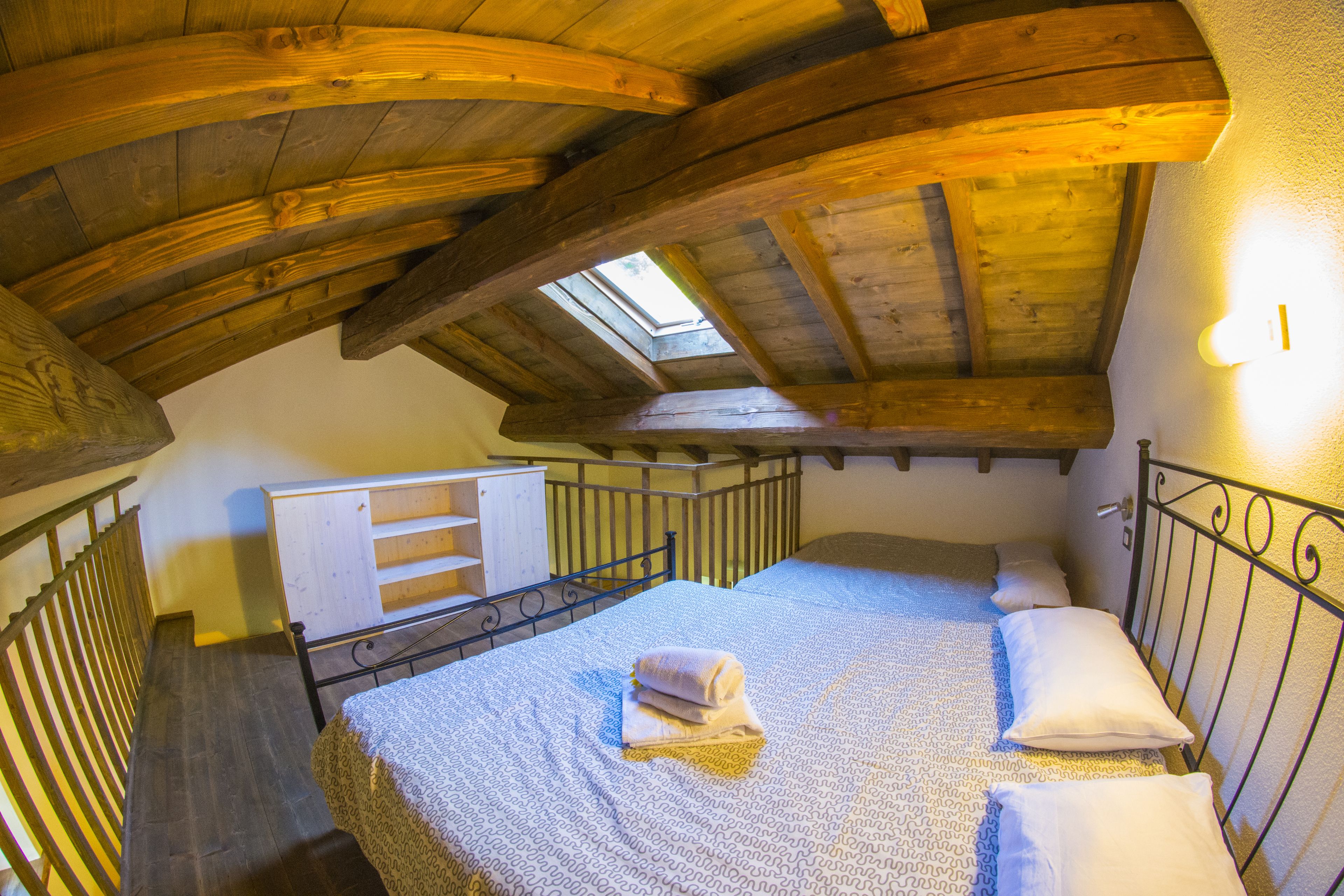 Een slaapkamer in een houten zolder met dakraam, een bed en een klein dressoir.