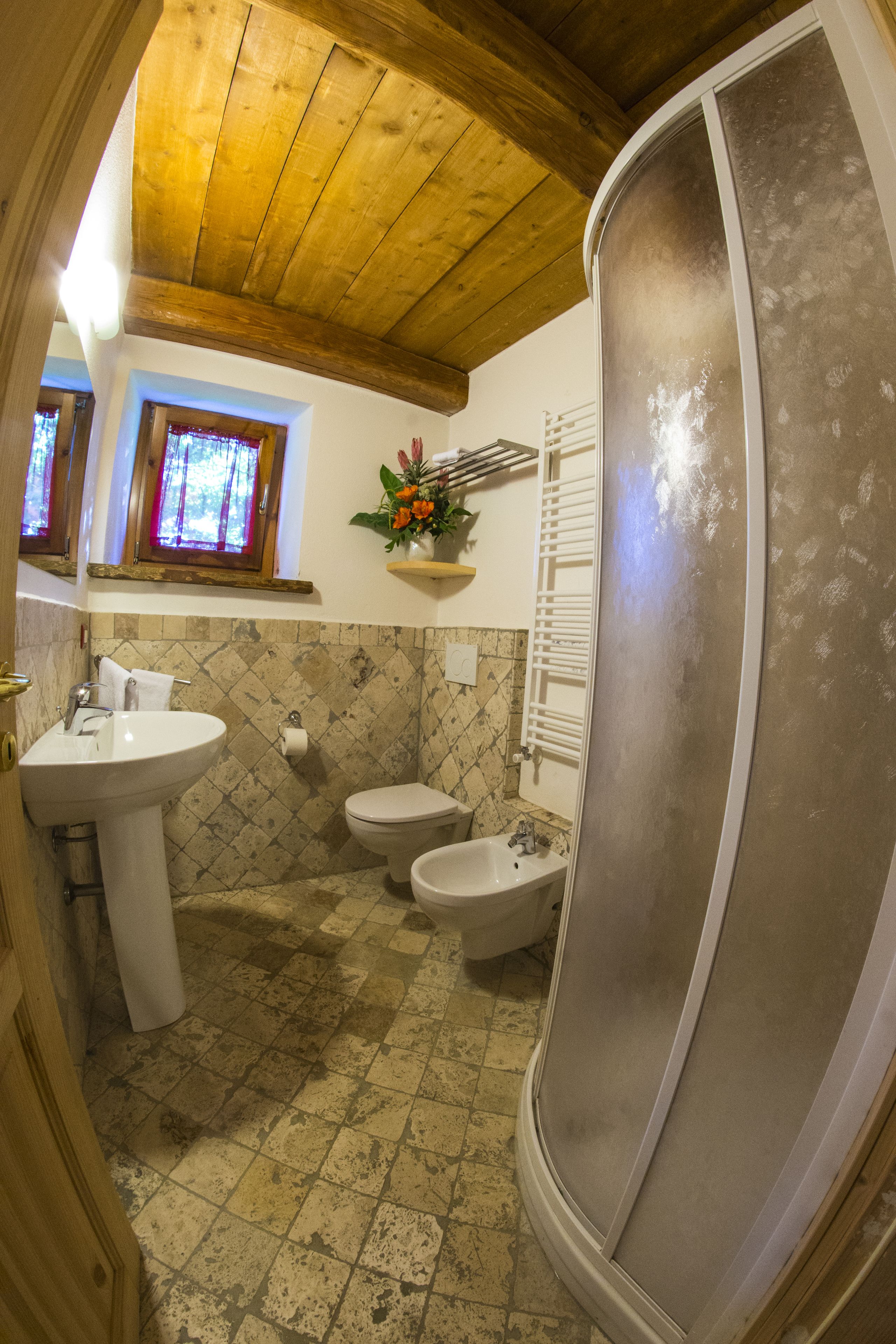 Een badkamer met een houten plafond, een wastafel, een toilet en een bidet.