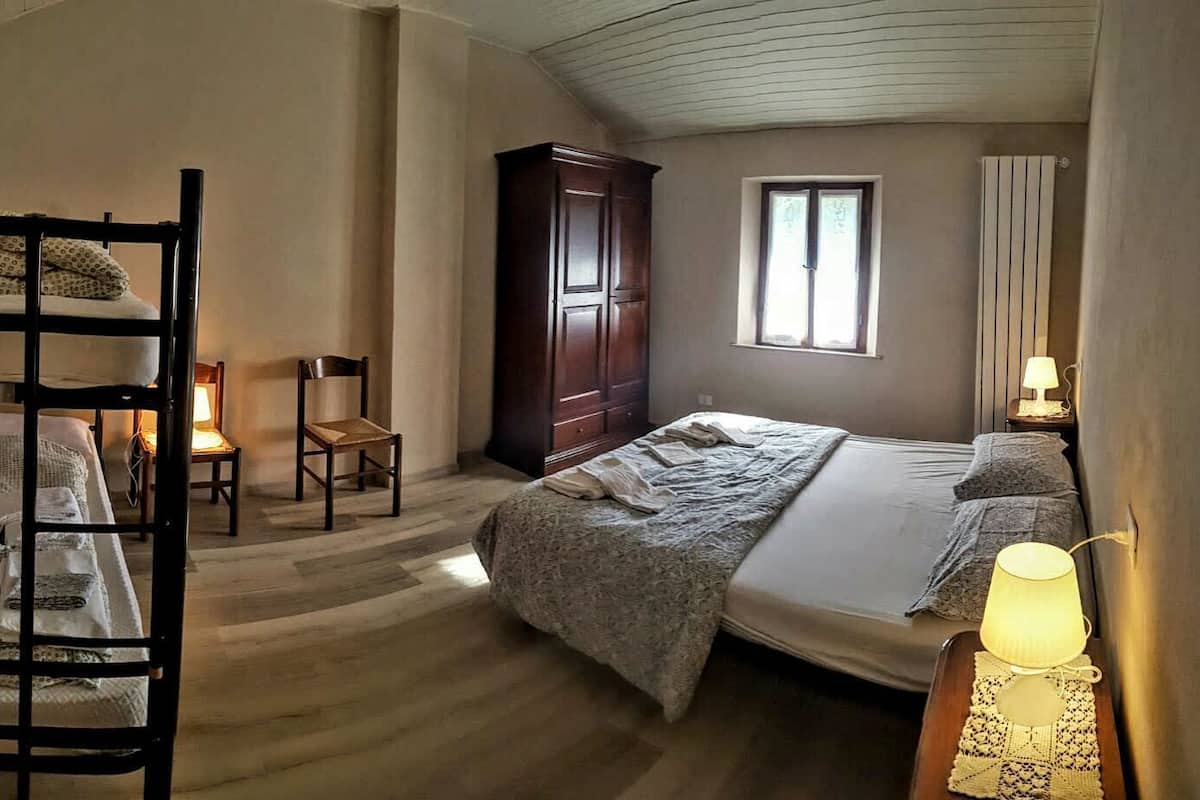 Une chambre avec des lits superposés, une armoire en bois, un bureau avec une lampe et une fenêtre avec des rideaux.