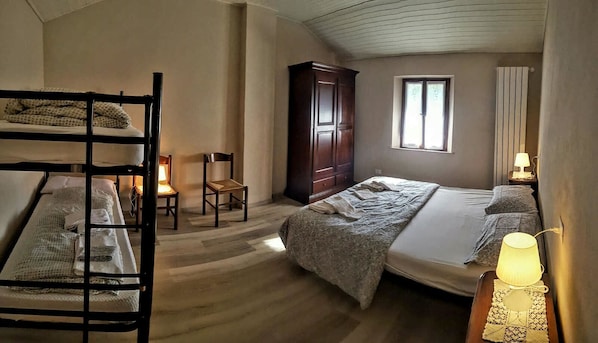 Quarto com beliches, um guarda-roupa de madeira, uma escrivaninha com luminária e uma janela com cortinas.