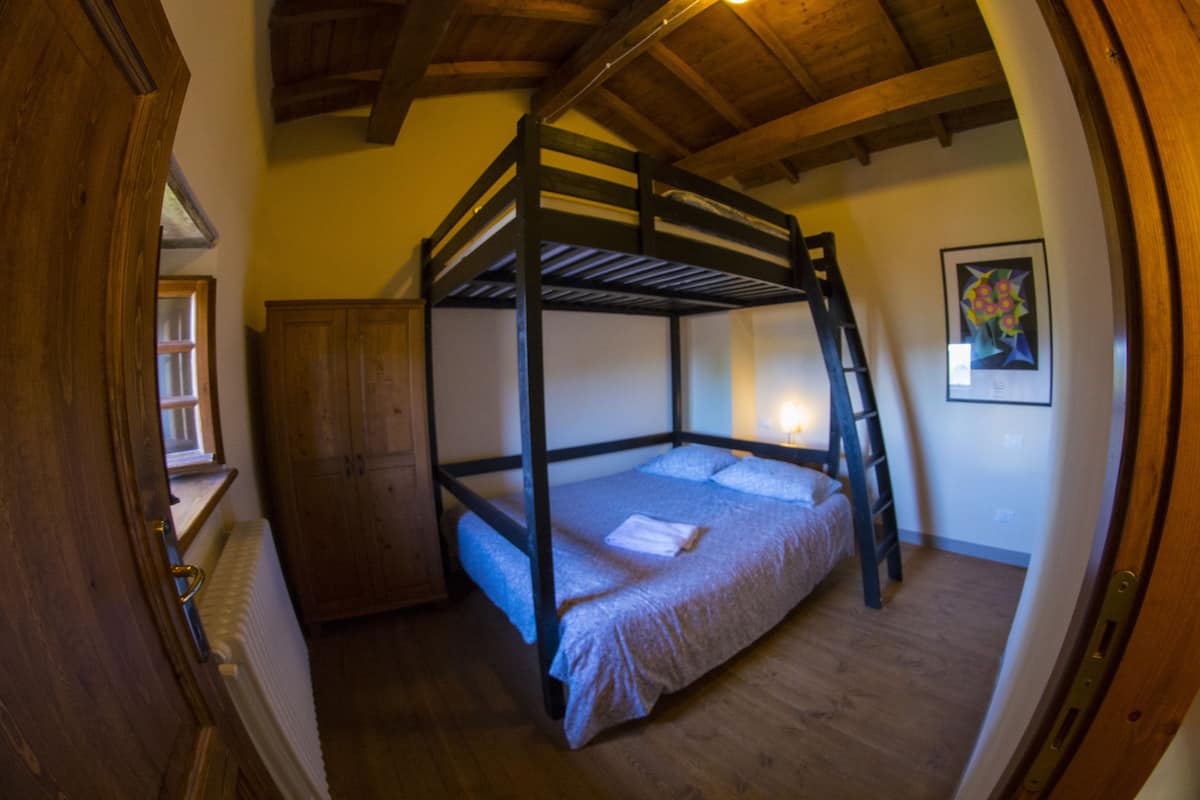 Une chambre avec un lit superposé, des poutres en bois, une échelle, une armoire en bois et un tableau encadré au mur.