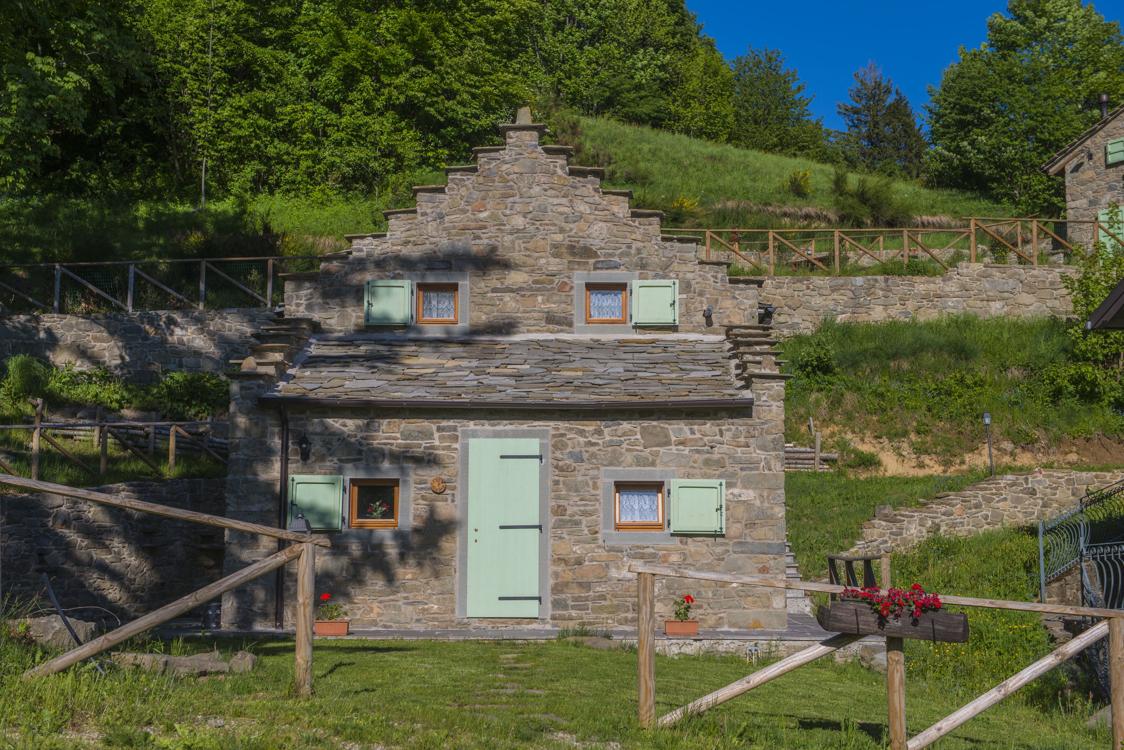 A stone cottage with a steep roof, a wooden fence, and a small garden with flowers.