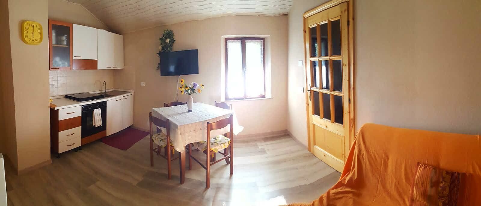 Una cucina compatta con mobili bianchi, lavastoviglie integrata e un tavolo con sedie.