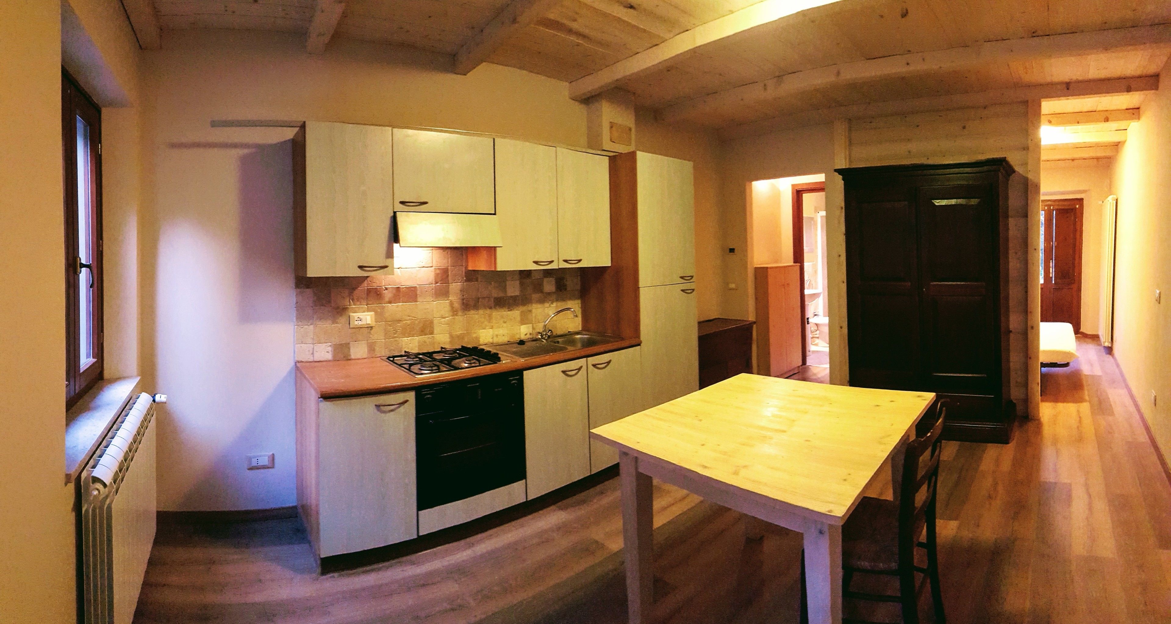 A compact kitchen with a gas stove, sink, and wooden cabinets. A small table is positioned in the center.