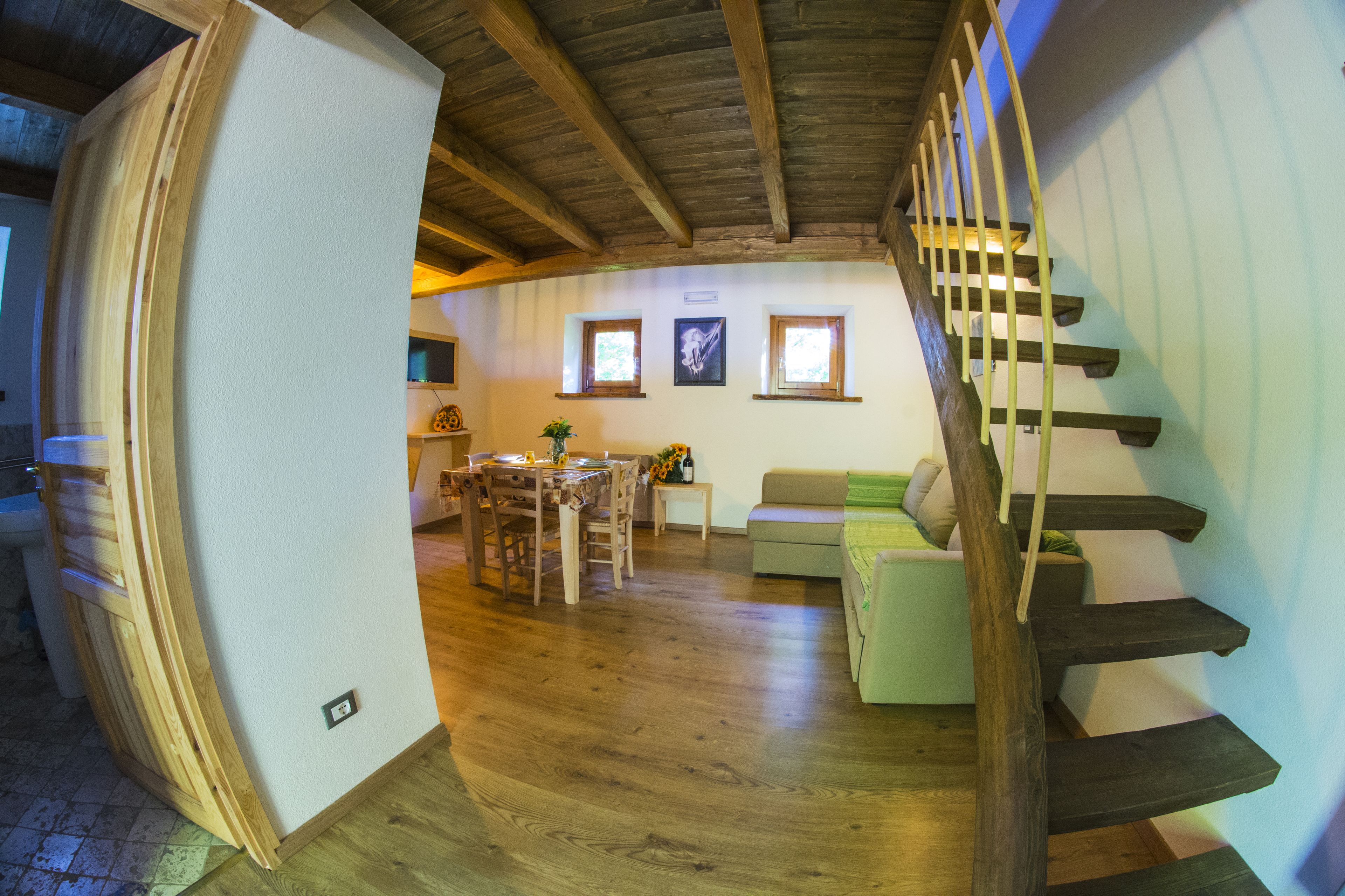 Amplia sala de estar con escalera de madera, una mesa de comedor con sillas y un sofá.