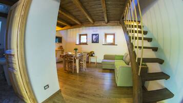 Amplia sala de estar con escalera de madera, una mesa de comedor con sillas y un sofá.