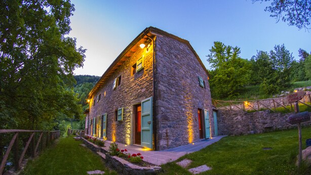 Une maison en pierre dotée de nombreuses portes et fenêtres, entourée d’un jardin bien entretenu et d’une clôture en bois.
