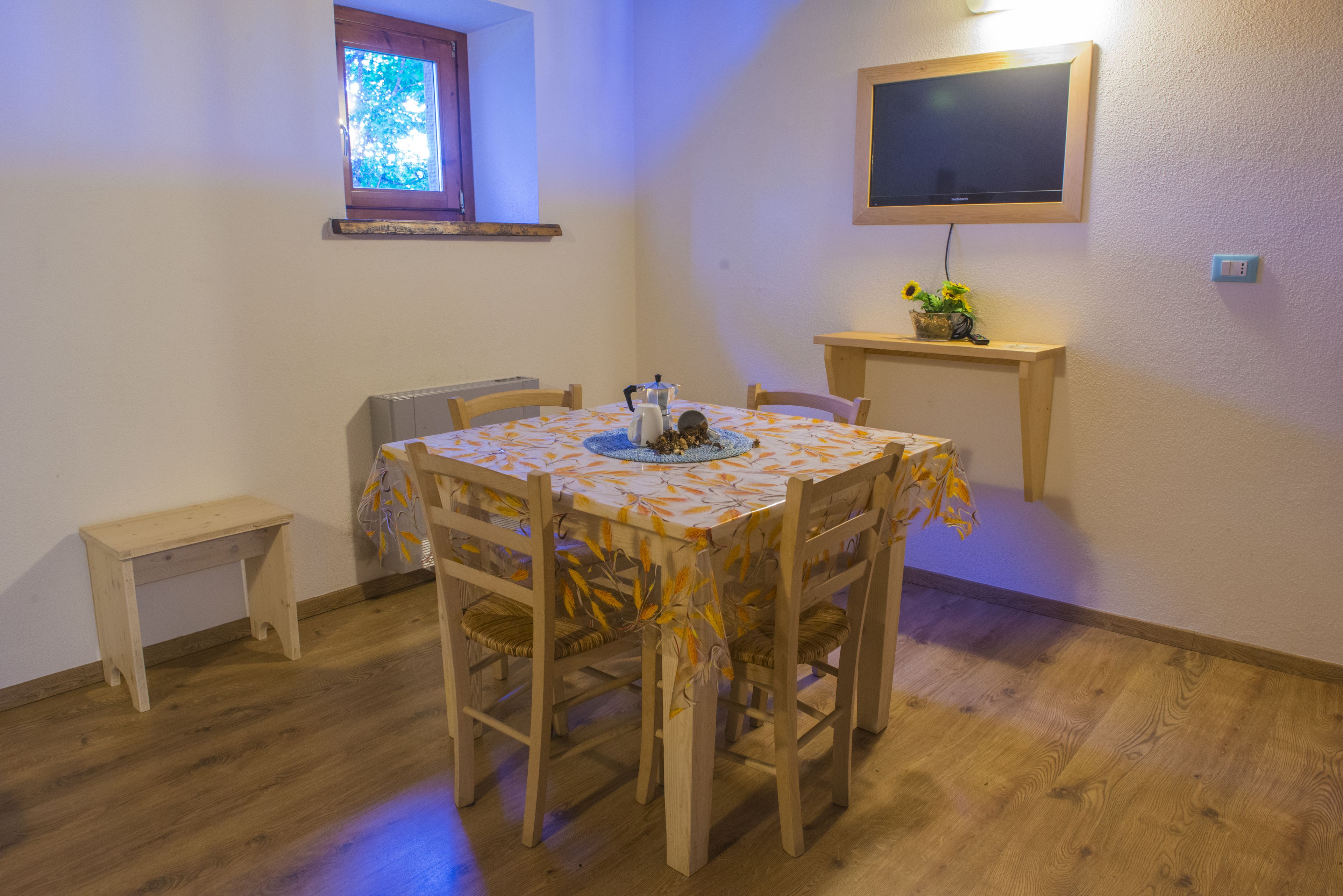 A dining area with a table covered in a floral tablecloth, surrounded by wooden chairs.