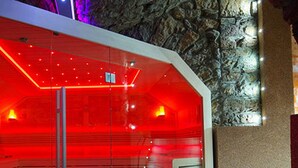 Uma sala de spa moderna com estrutura de vidro, iluminação vermelha e parede de pedra como cenário.