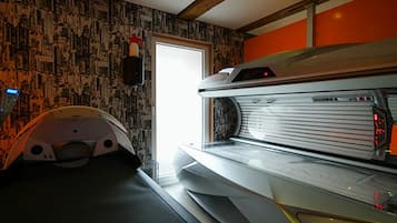 A tanning bed in a room with patterned wallpaper and a door leading to an adjacent room.