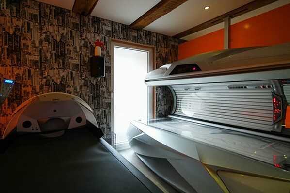 Una cama bronceadora en una habitación con papel tapiz estampado y una puerta que da a otra sala.