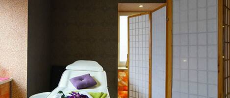 Una habitación con una camilla de masaje, techo de madera y una puerta corredera.