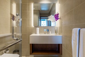 A modern bathroom with a glass shower enclosure, a white sink, and a mirror above it. - Deluxe Holiday Homes - Marina Gate (Dubai)