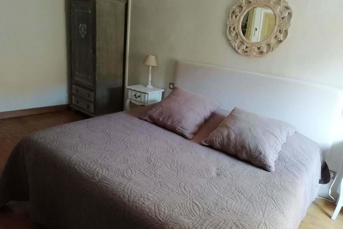 Een slaapkamer met een bed, een dressoir, een nachtkastje, een lamp en een spiegel.