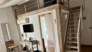 Een slaapkamer in loftstijl met een houten trap, een bureau met een flatscreen televisie en een stoel.