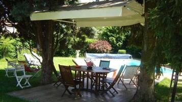 Um pátio externo com mesa e cadeiras, cercado por árvores e uma piscina.