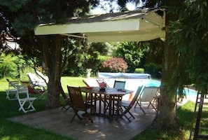 Un patio al aire libre con una mesa y sillas, rodeado de árboles y una piscina.